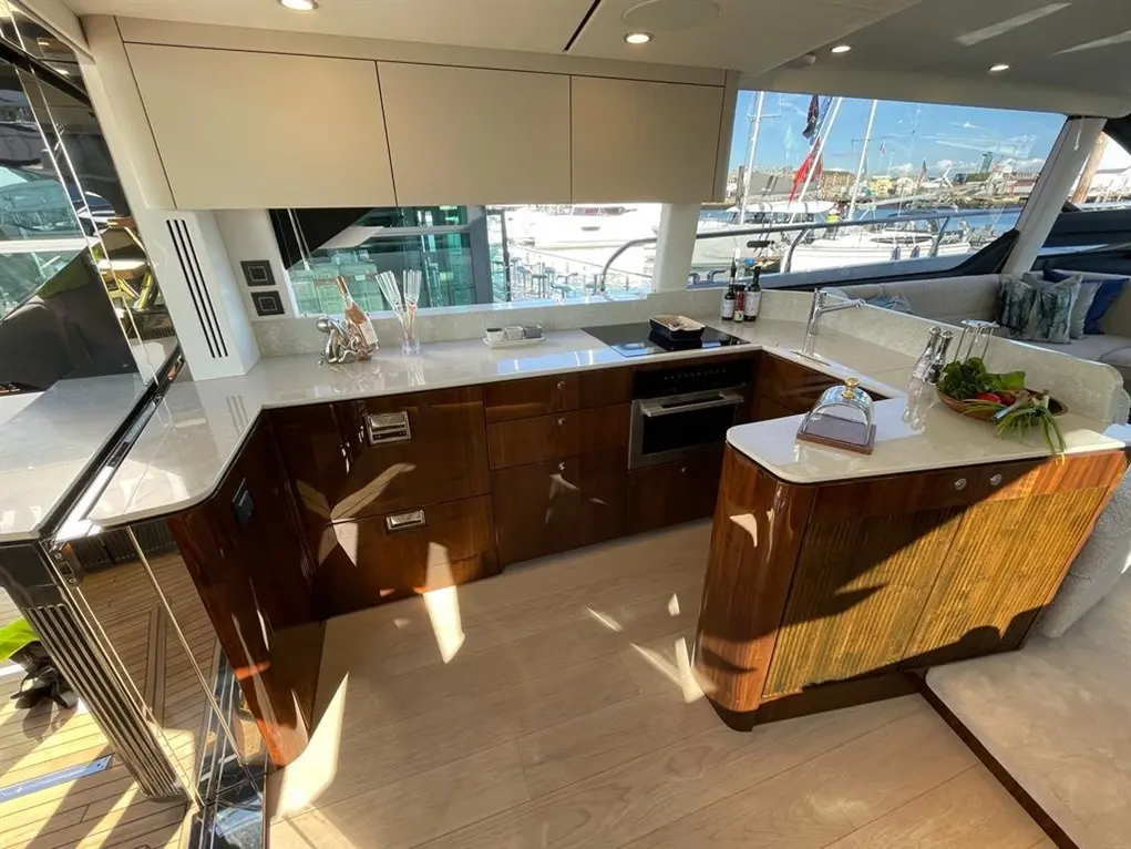 Luxury yacht kitchen with wooden cabinets, a marble countertop, and a view of the marina with moored boats outside.